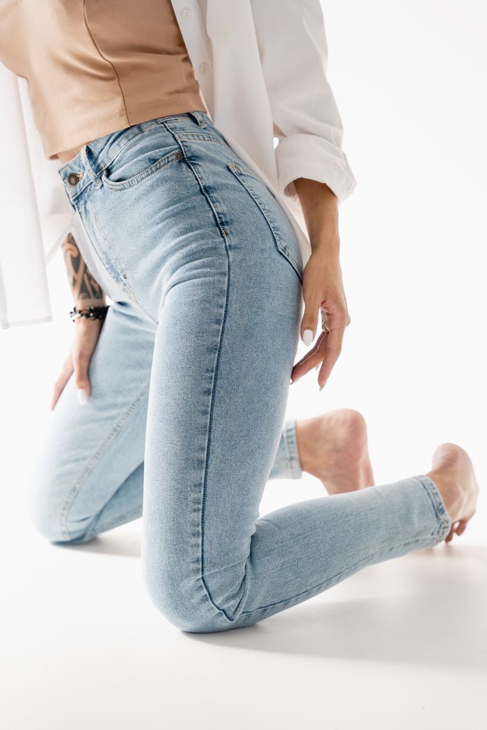 services-04 Close-up of a woman kneeling in light blue jeans with a neutral top and white background.