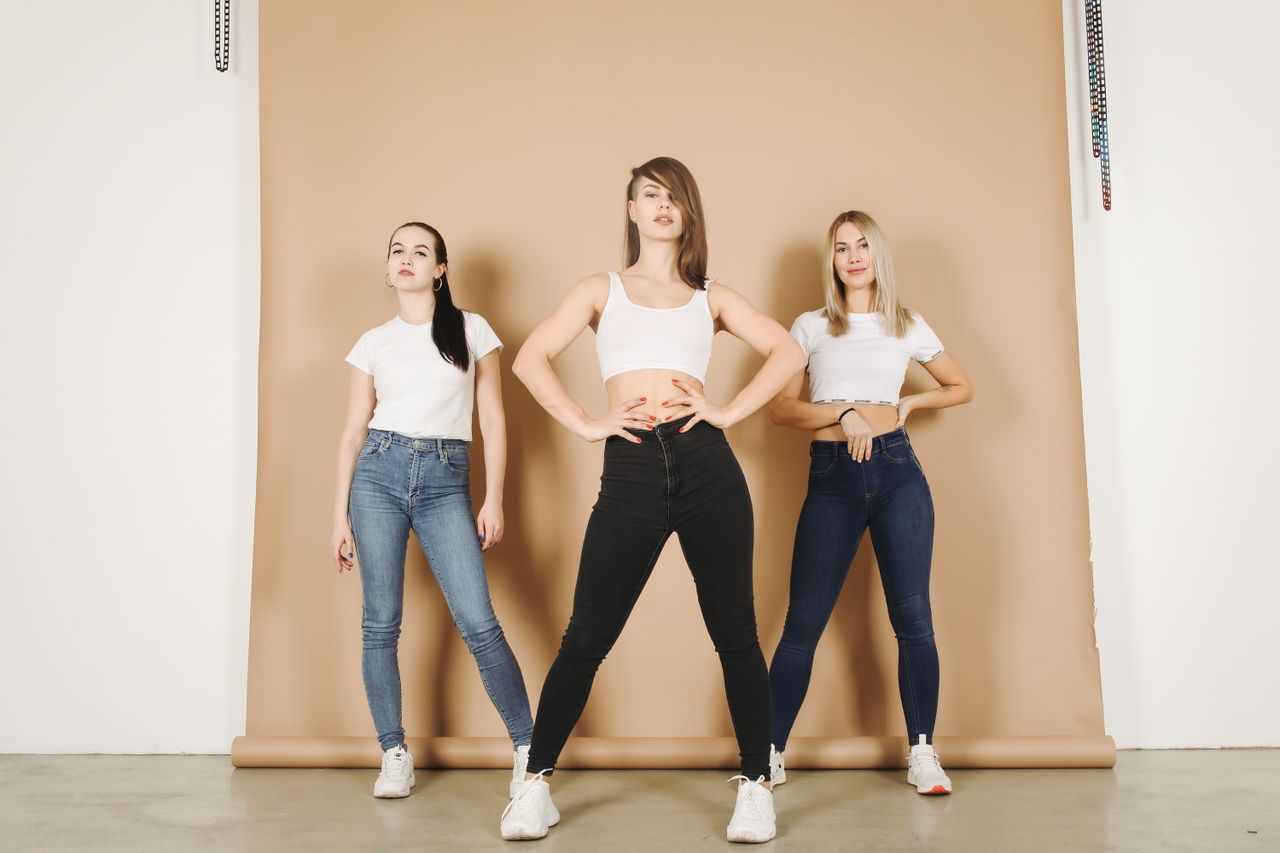 Three women in casual denim outfits posing confidently in a studio setting.